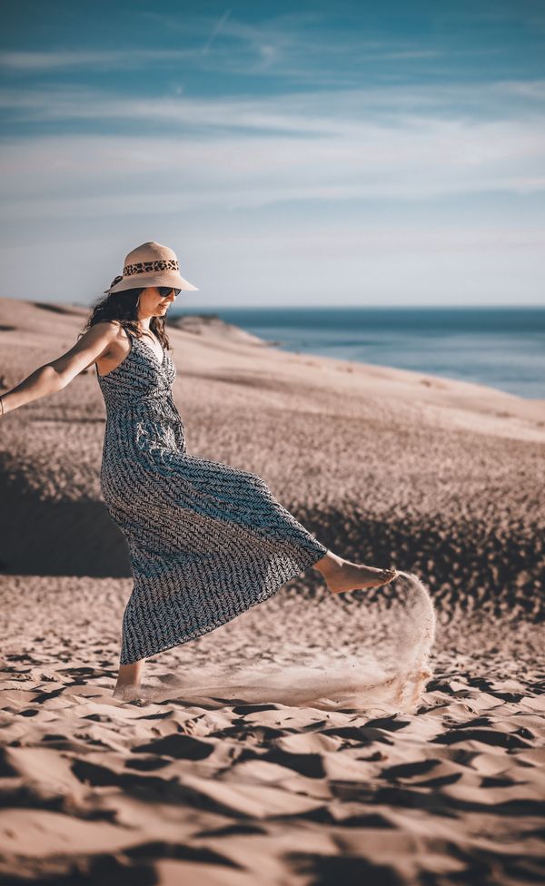 A woman in a wide-brimmed hat walking through coastal dunes — photo by Nicolas Lesueur on Pexels