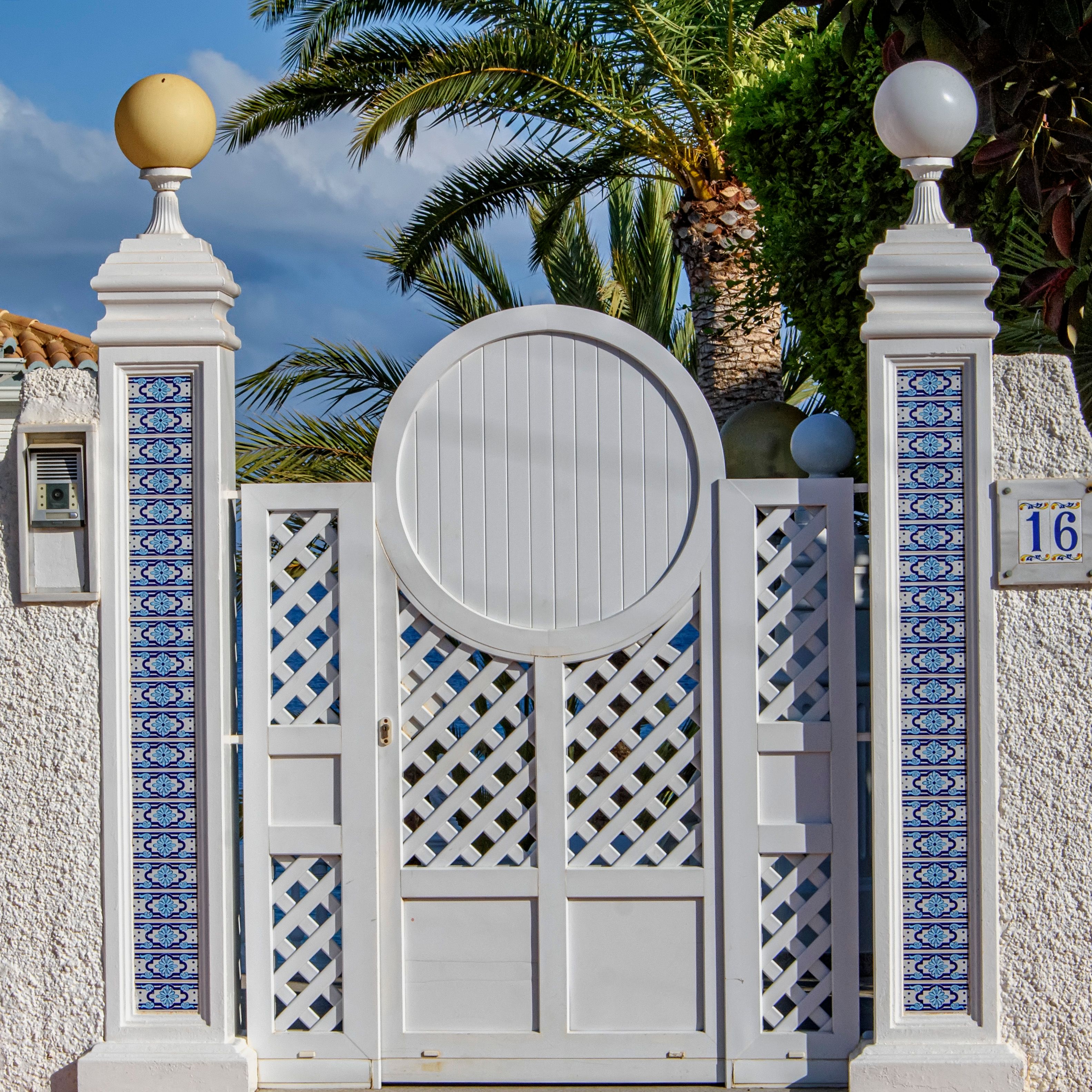 Elegant white gate with colorful tiles, palm trees in the background in El Campello, Spain.