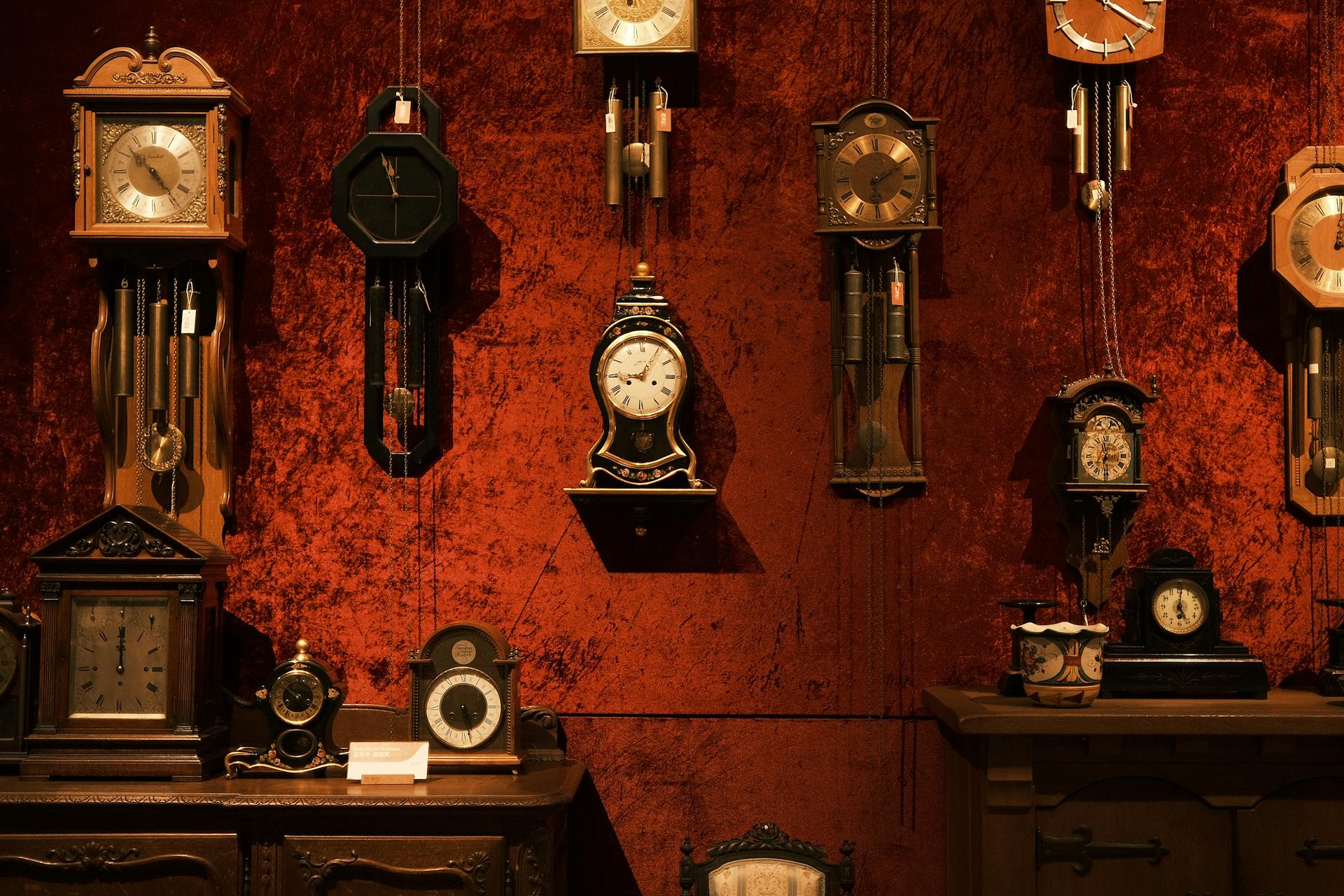 A charming collection of vintage clocks on a red velvet wall, showcasing timeless elegance.