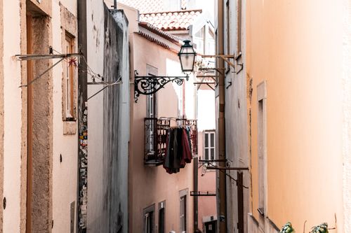Free Narrow urban alley lined with European architecture, featuring hanging clothes and a vintage street lamp. Stock Photo