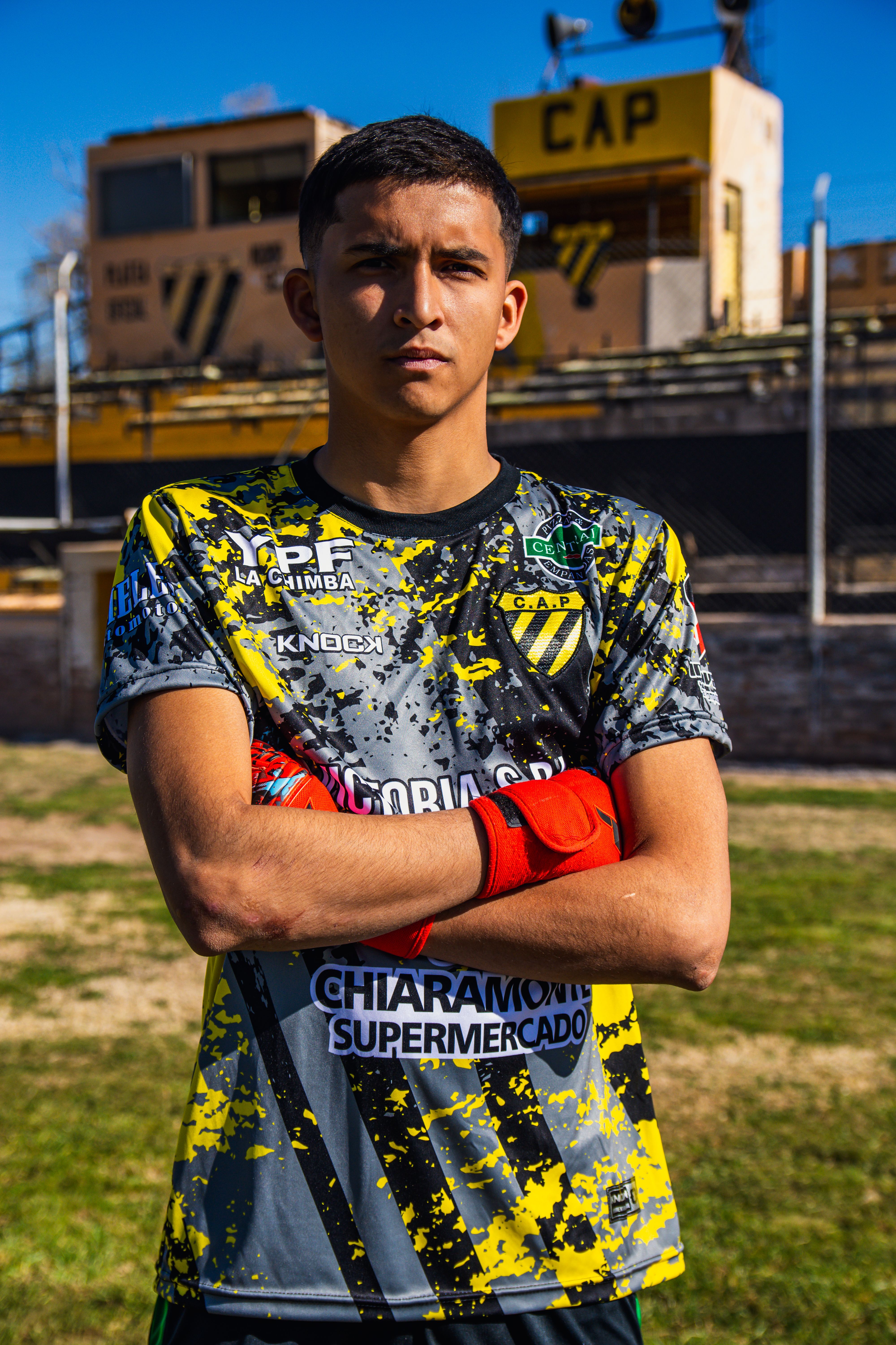 Teen soccer player poses confidently in a vibrant team jersey on a sunny day.