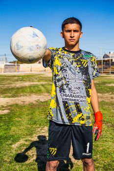 A young soccer player stands on the field holding a ball, ready to play.