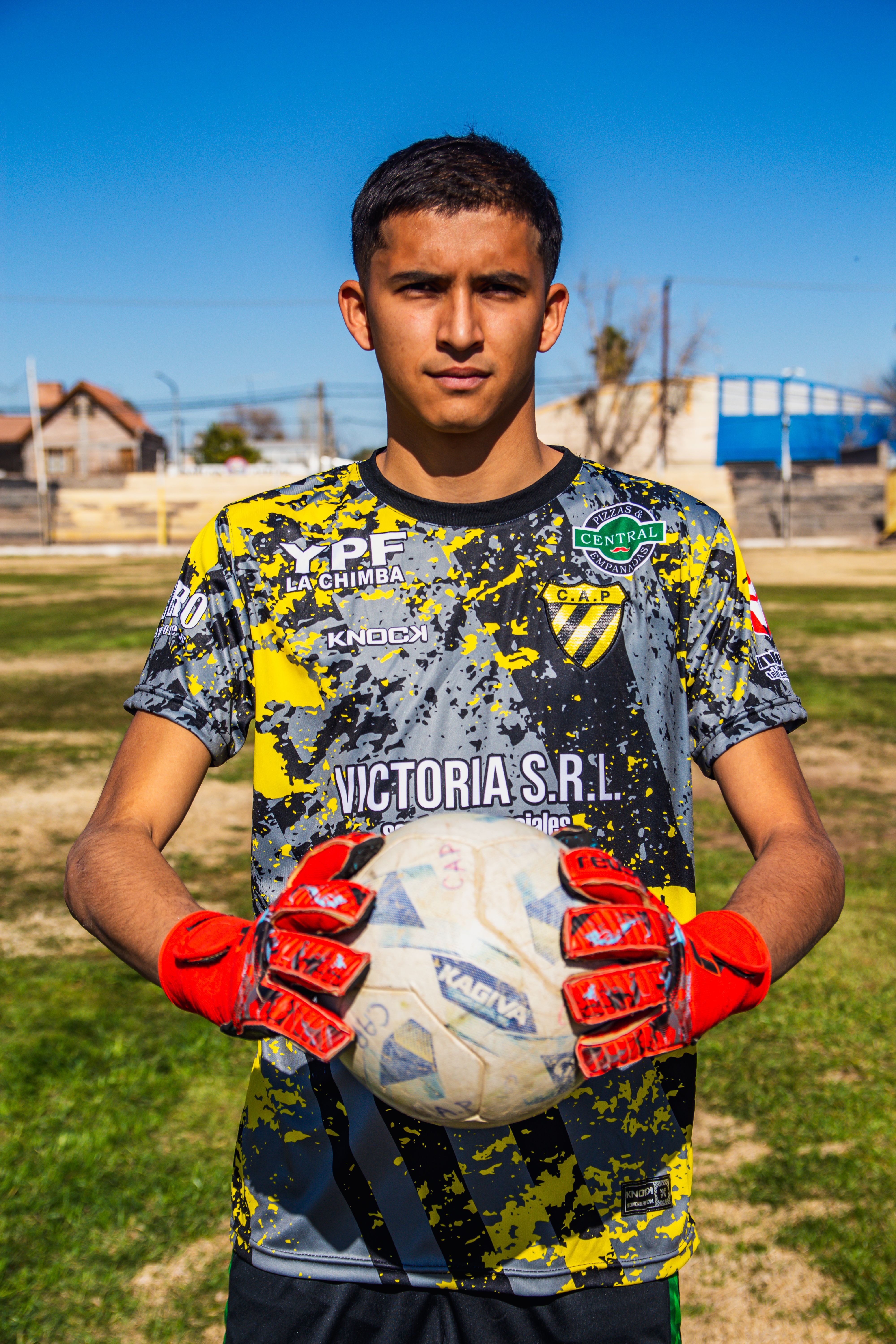 Teen soccer player outdoors holding a ball in summer sports gear.