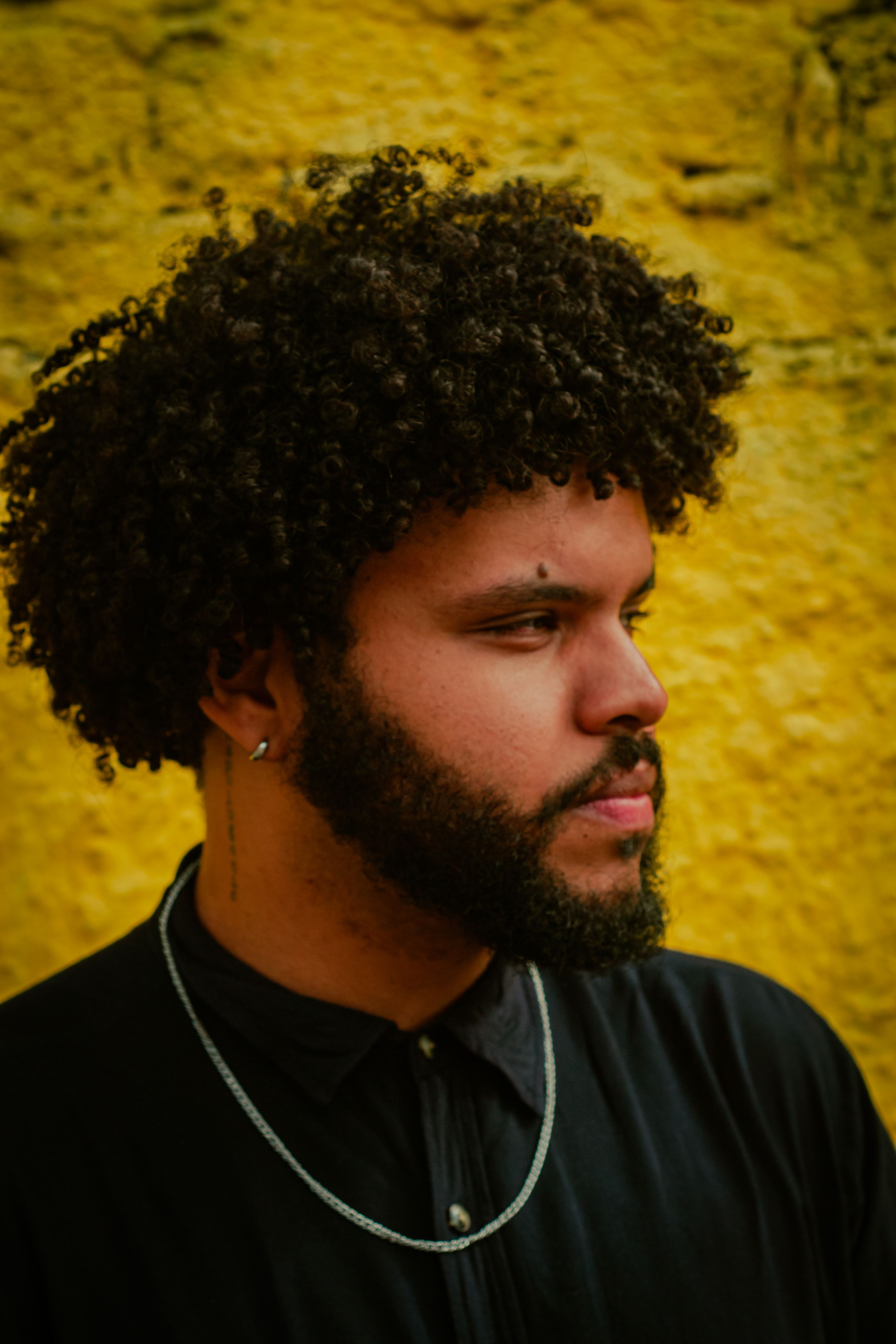 Close-up portrait of a man with afro hairstyle and beard against a textured yellow wall in Recife, Brazil.