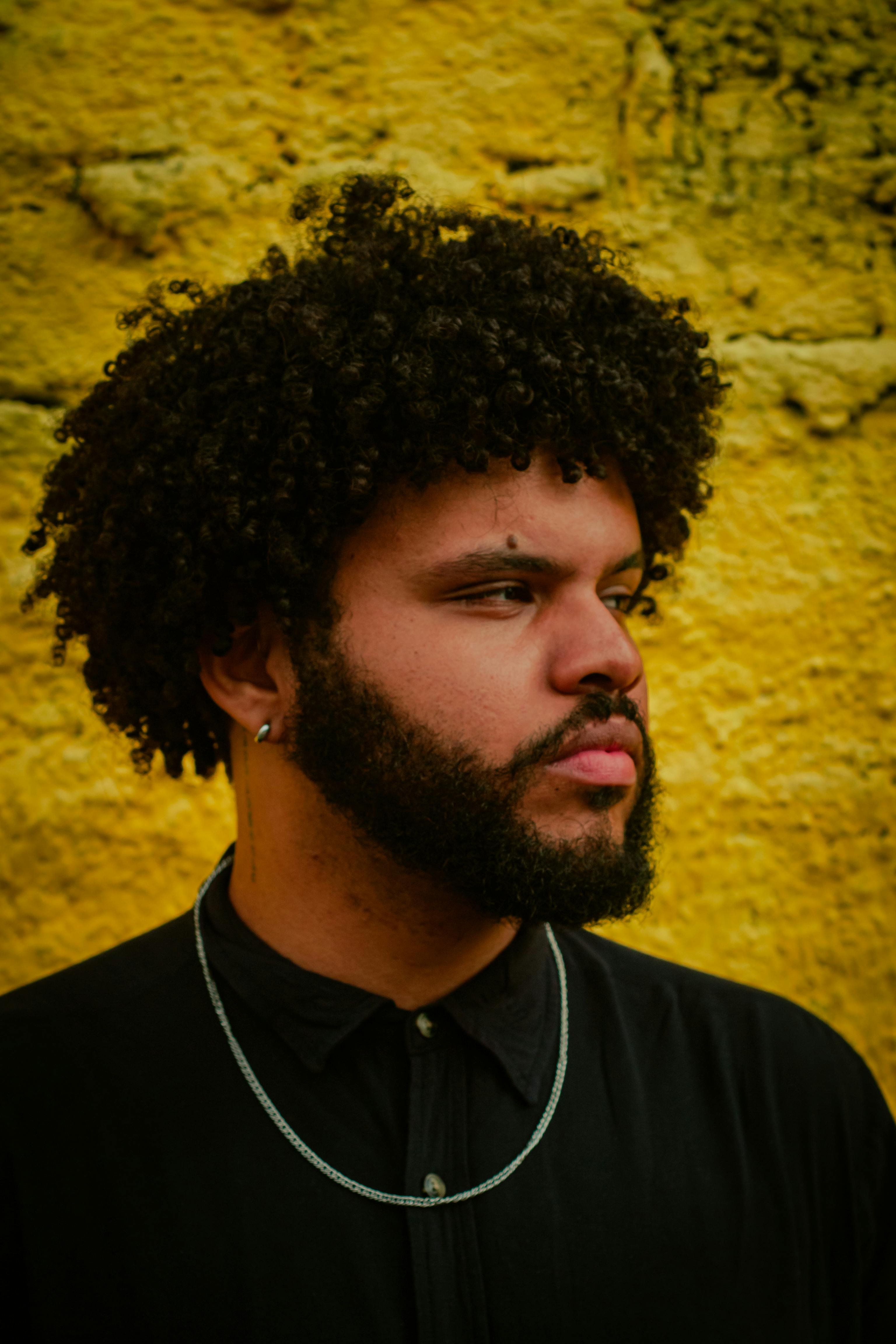 Portrait of a confident man with curly hair against a vibrant yellow wall in Recife, Brazil.