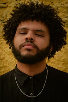 Close-up portrait of a man with curly hair and beard against a textured wall.