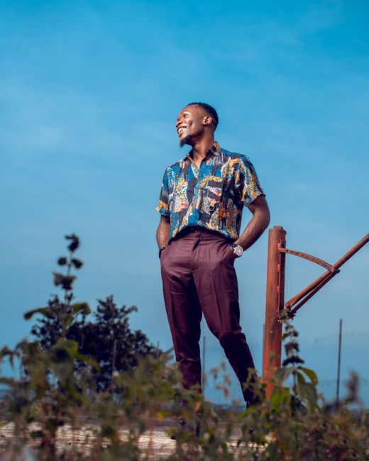 A cheerful young man in a colorful shirt stands outdoors under a clear blue sky. A cheerful young man in a colorful shirt stands outdoors under a clear blue sky.