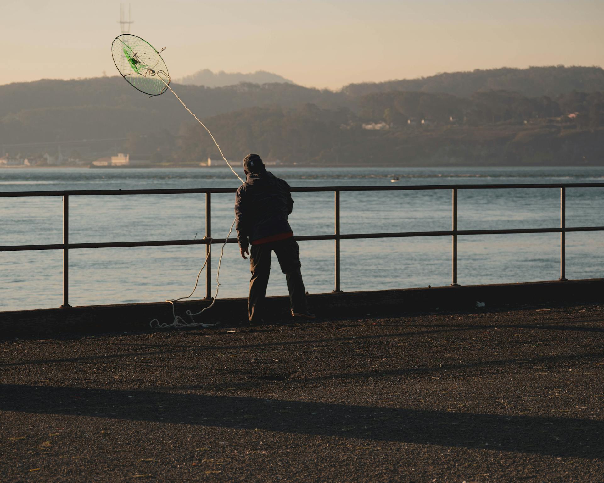 A fisherman on the San Francisco Bay pier casting a net during sunrise.