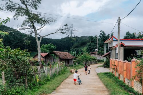 Free A serene village road with children playing and a scenic background. Stock Photo