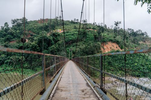 Free A rustic suspension bridge crossing a river in a lush, hilly landscape. Stock Photo