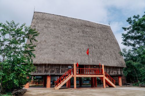 Free A rural Vietnamese house with a thatched roof and red accents, surrounded by greenery. Stock Photo