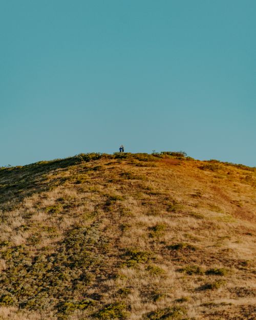 Free Two hikers standing on a hill under a clear blue sky at sunrise in San Francisco. Stock Photo