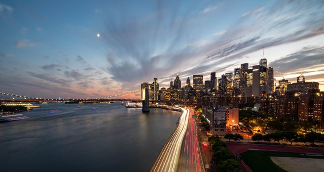 Stunning twilight view of New York City skyline with Brooklyn Bridge and light trails.