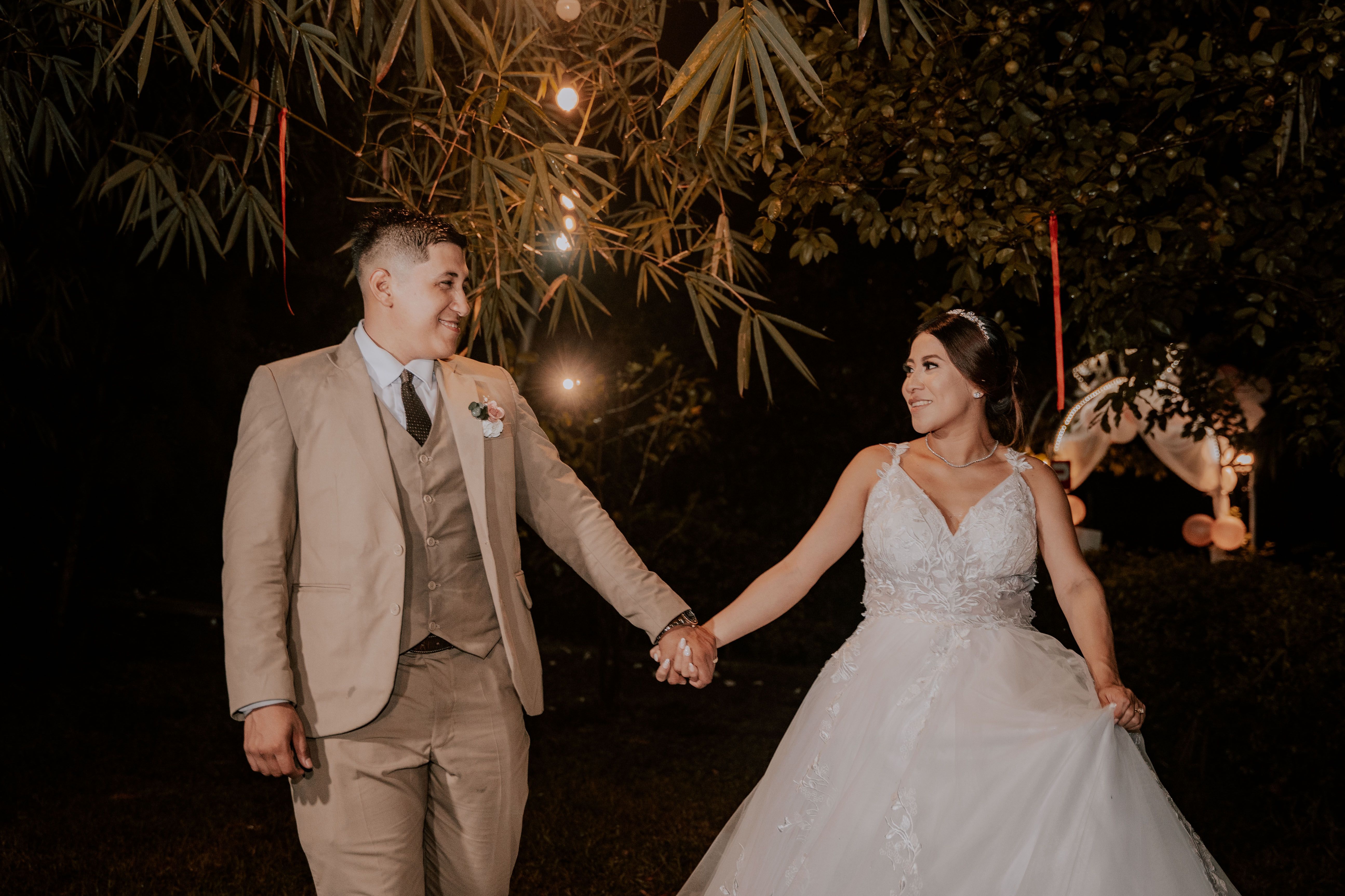 A bride and groom holding hands under a tree · Free Stock Photo