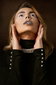 Striking portrait of a woman with pearl embellishments and artistic makeup wearing a stylish black outfit.