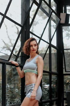 一位时尚女性身着运动服，站在大窗户旁，展现了现代健身与城市生活方式