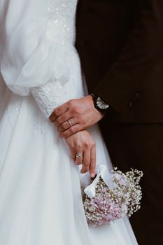 A close-up of newlyweds holding hands, showcasing rings and a delicate bouquet with a classic touch.