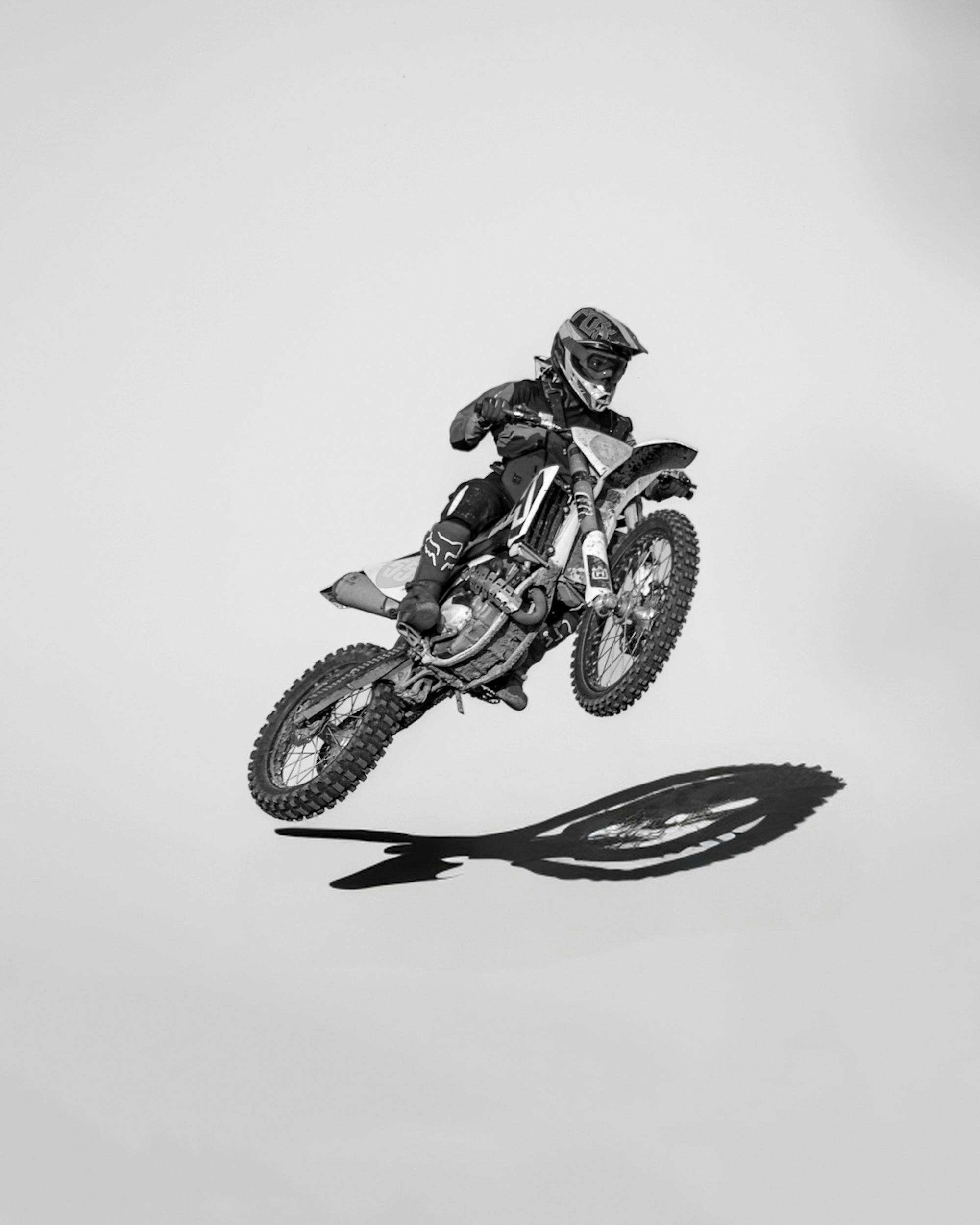 Monochrome image capturing a motocross rider's high-flying jump against a white background.