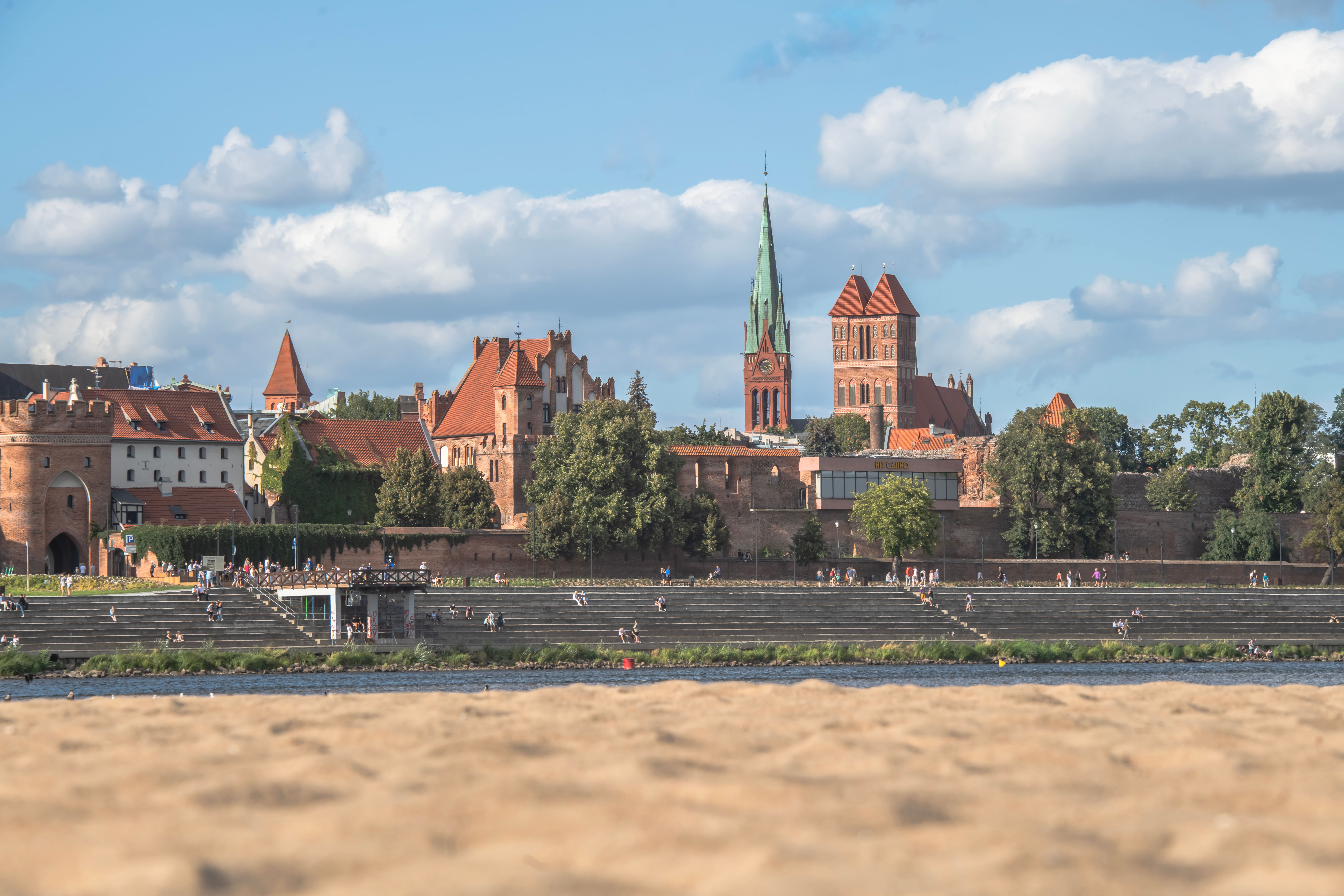 Charming view of a medieval town by the river with towers and vibrant summer skies. — Trójmiasto