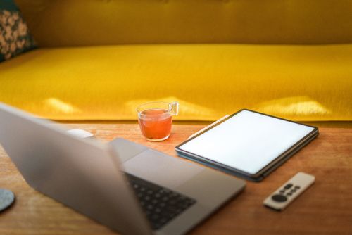 Free Cozy workspace with a laptop, tablet, and tea on a wooden table in a modern living room. Stock Photo