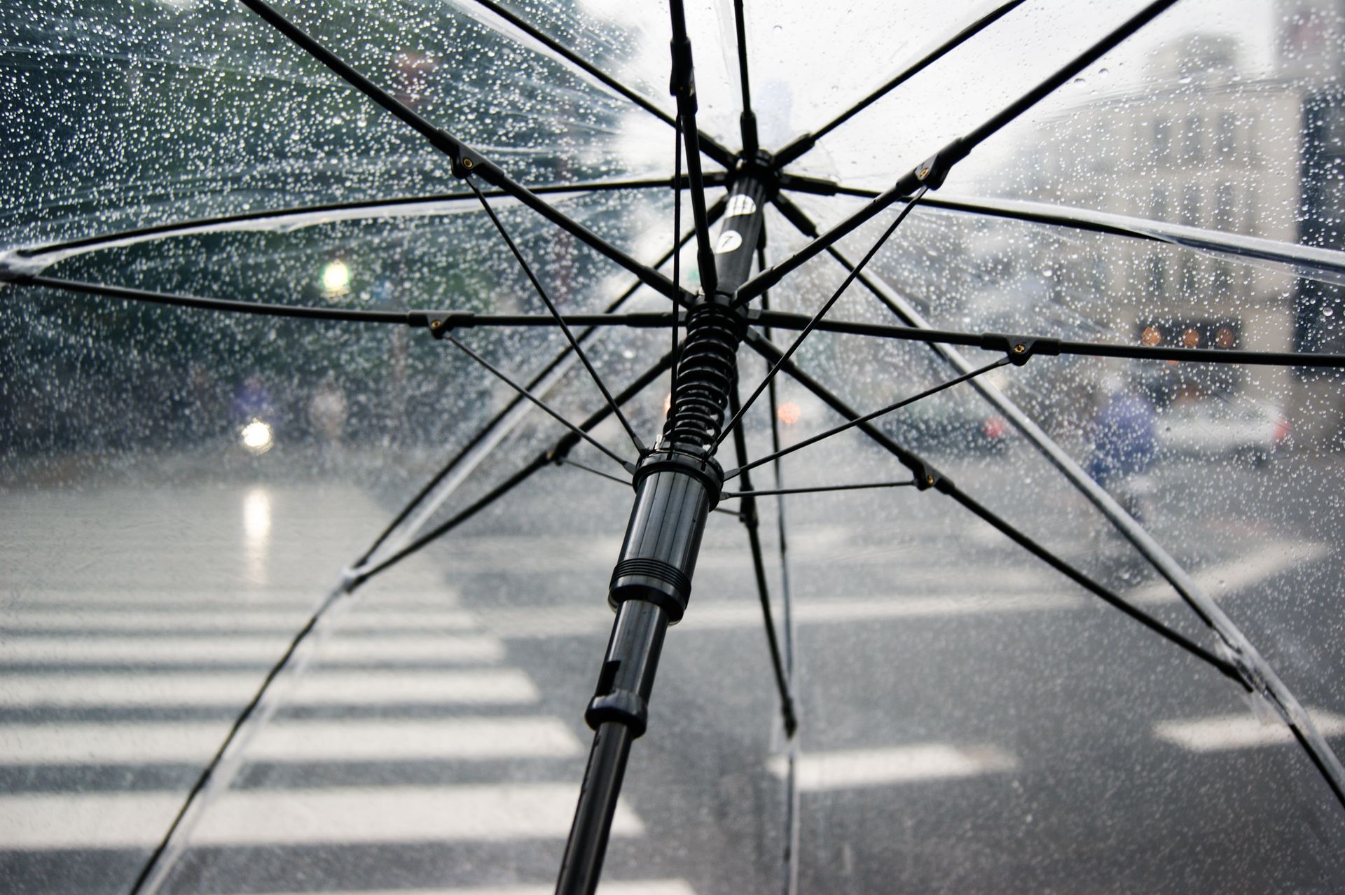 Close-up of a transparent umbrella with raindrops in an urban street setting.
