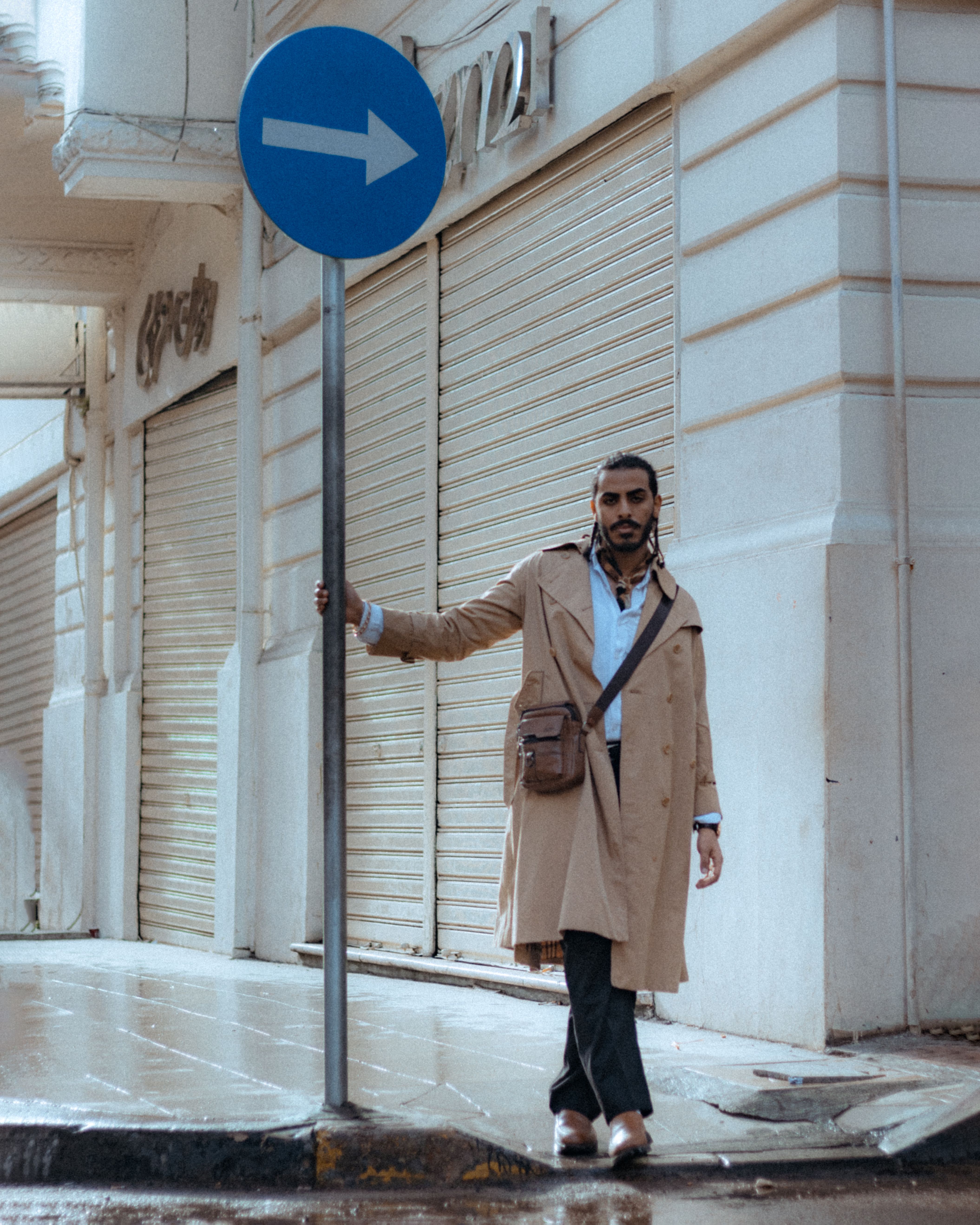 Elegant man poses on a rainy city street in Alexandria, Egypt, wearing a timeless trench coat.