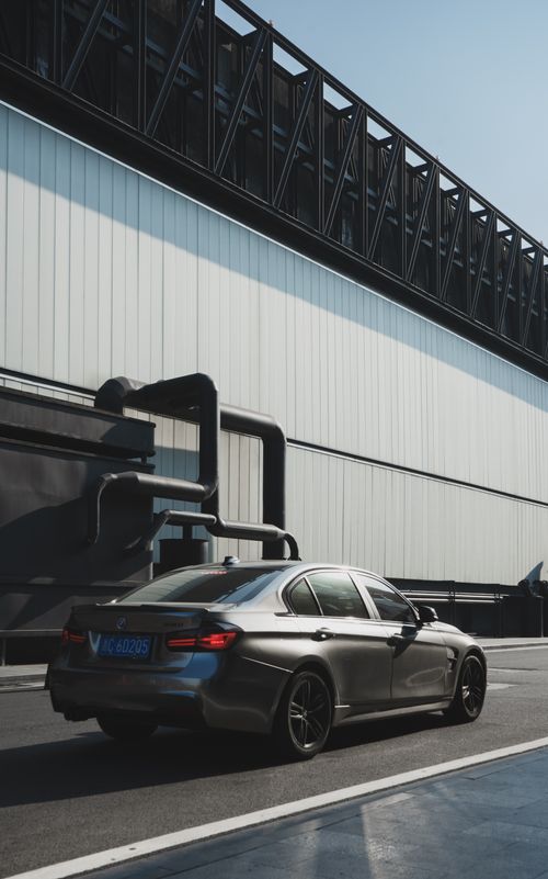 Free Sleek car driving along a city street with industrial backdrop during daylight. Stock Photo