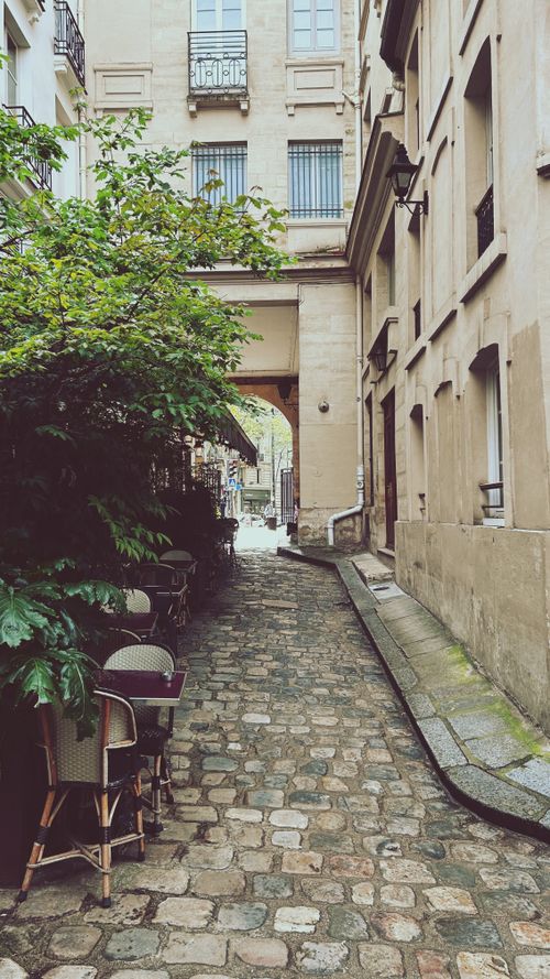Free Explore a quaint cobblestone alley with classic Parisian architecture and outdoor cafe seating. Stock Photo