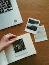 将即时照片用笔记本电脑整理到木制桌子的相册中