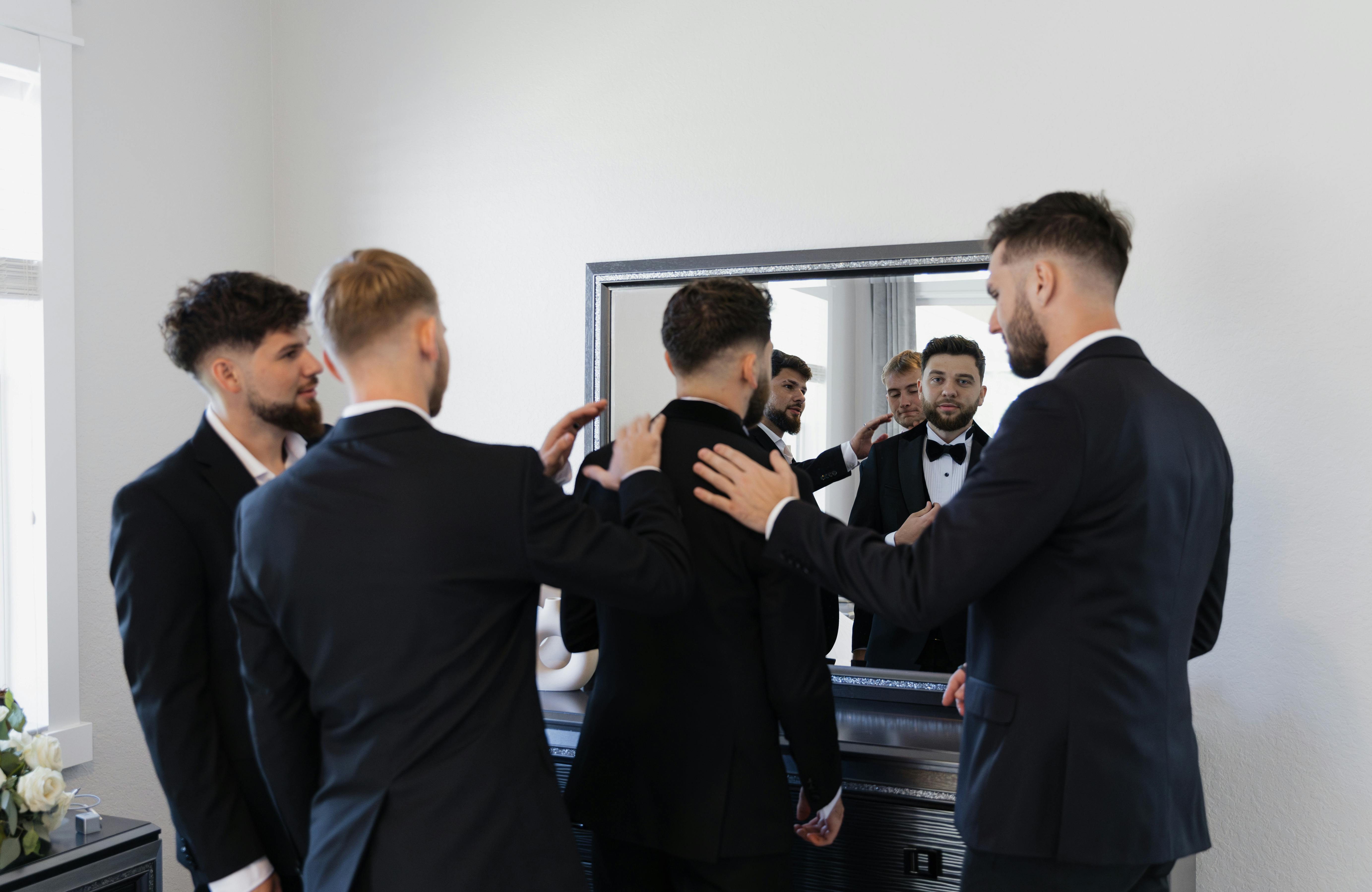 Groomsmen preparing suits in front of mirror for a wedding.