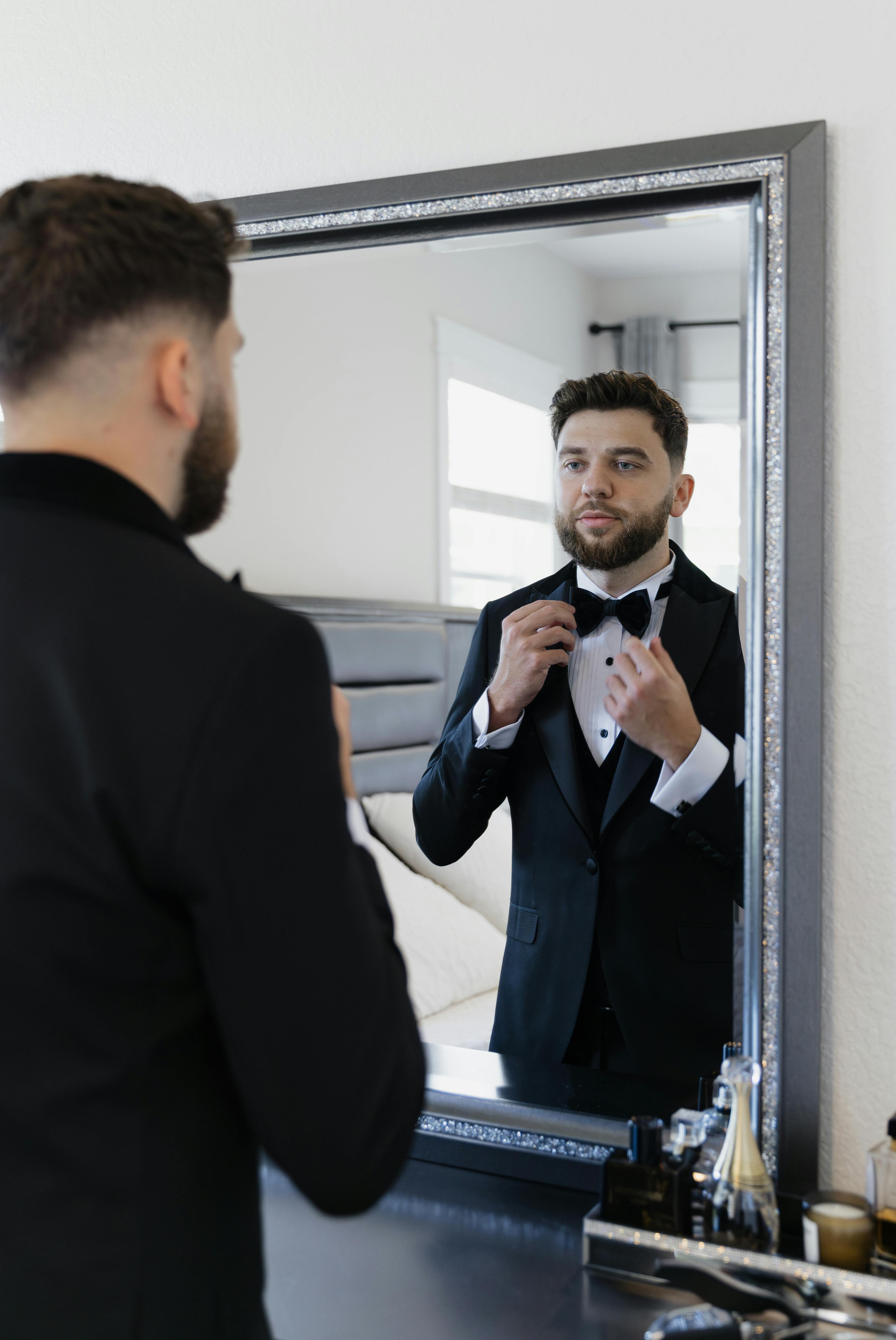 a man in a tuxedo is adjusting his bow tie