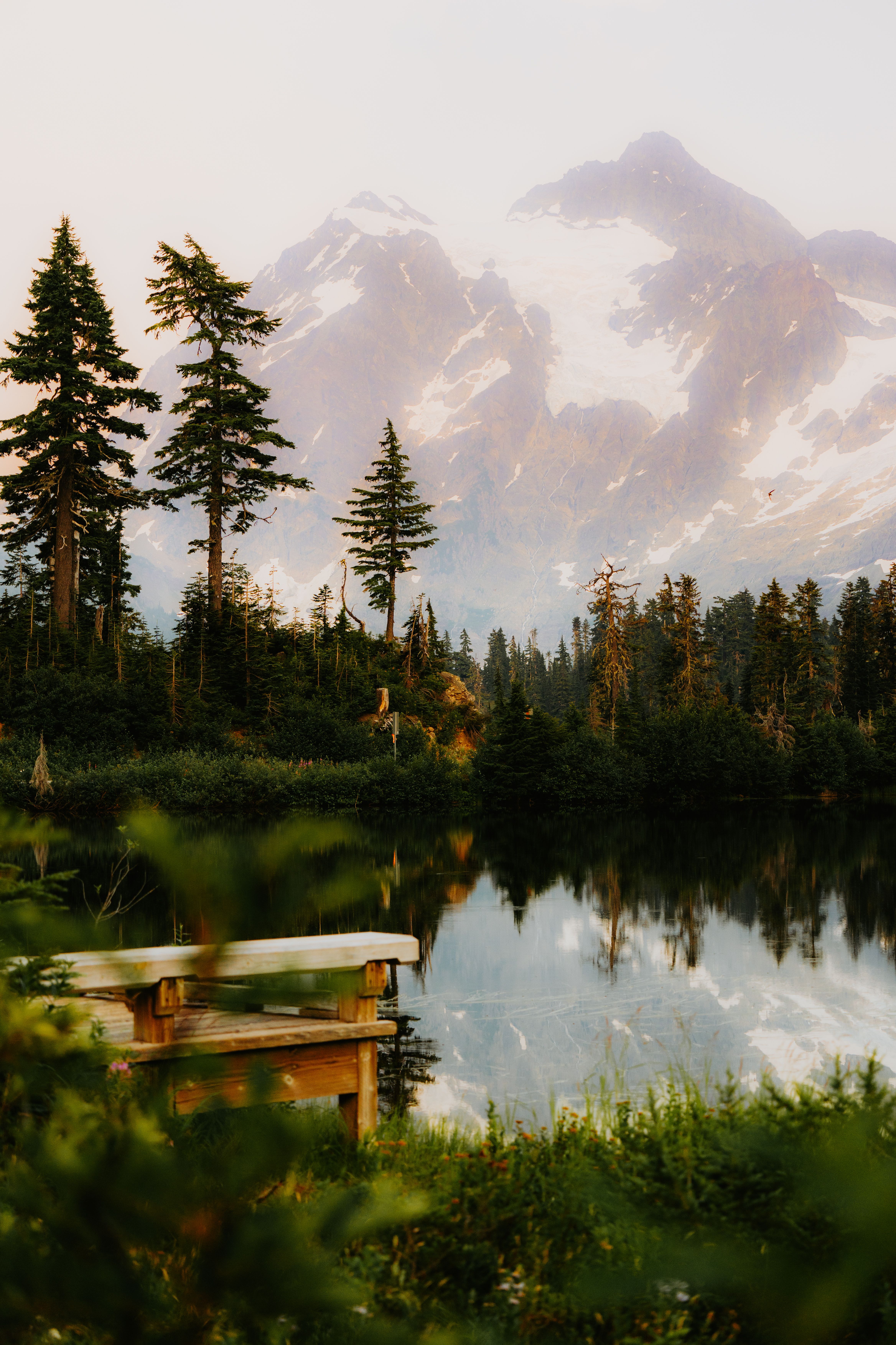 A bench sits on a lake with mountains in the background · Free Stock Photo