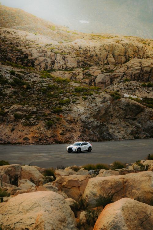 Free A car navigating a rugged, scenic road through dry rocky terrain under a warm glow. Stock Photo