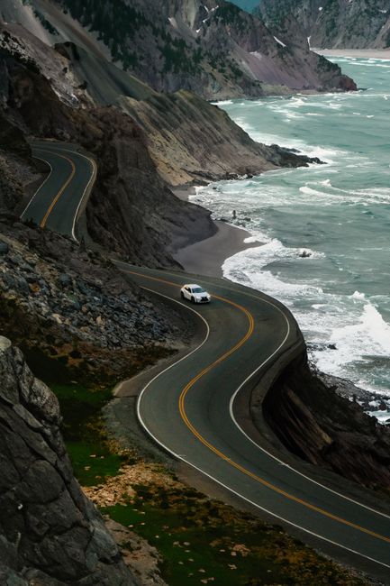 A white car navigating a winding road along a stunning coastal landscape.