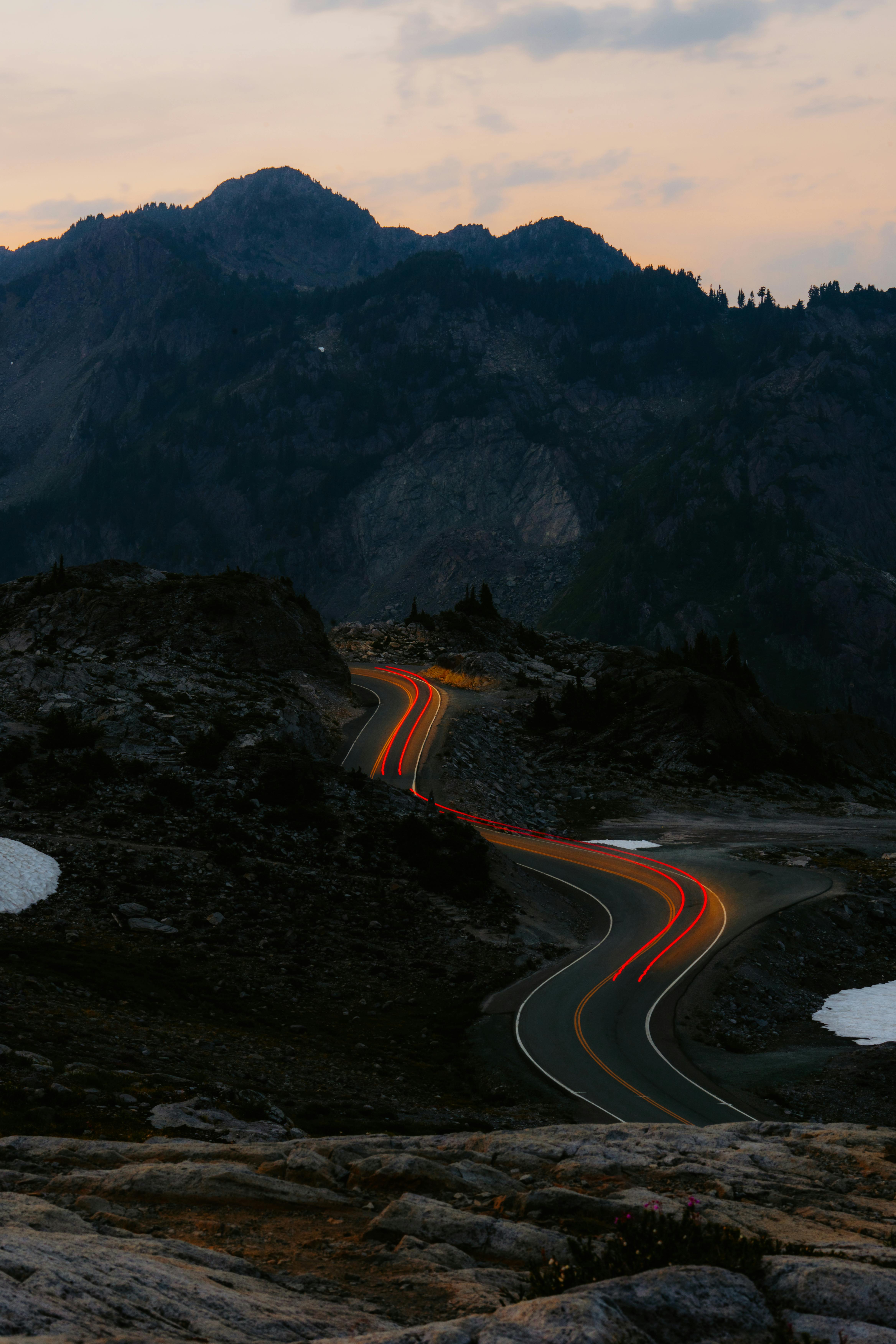 A scenic mountain road at twilight with car light trails and rugged terrain, perfect for travel and adventure themes.