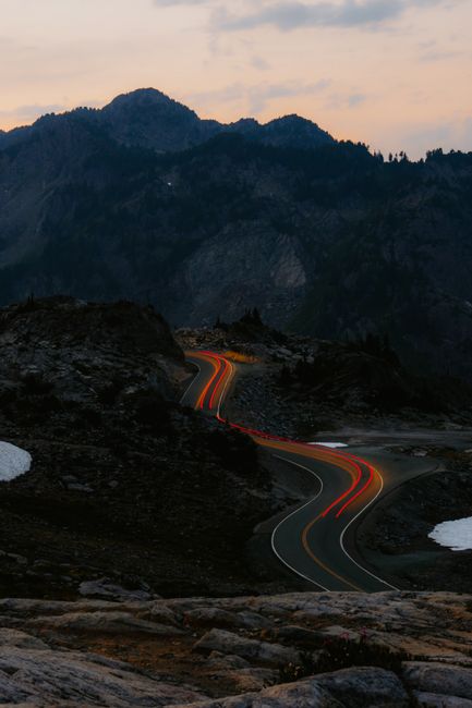 A scenic mountain road at twilight with car light trails and rugged terrain, perfect for travel and adventure themes.