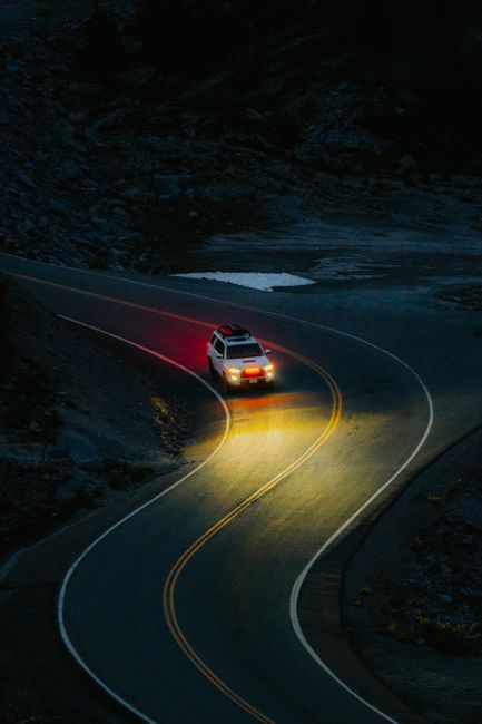 A white SUV navigating a winding mountain road under dark, atmospheric lighting.