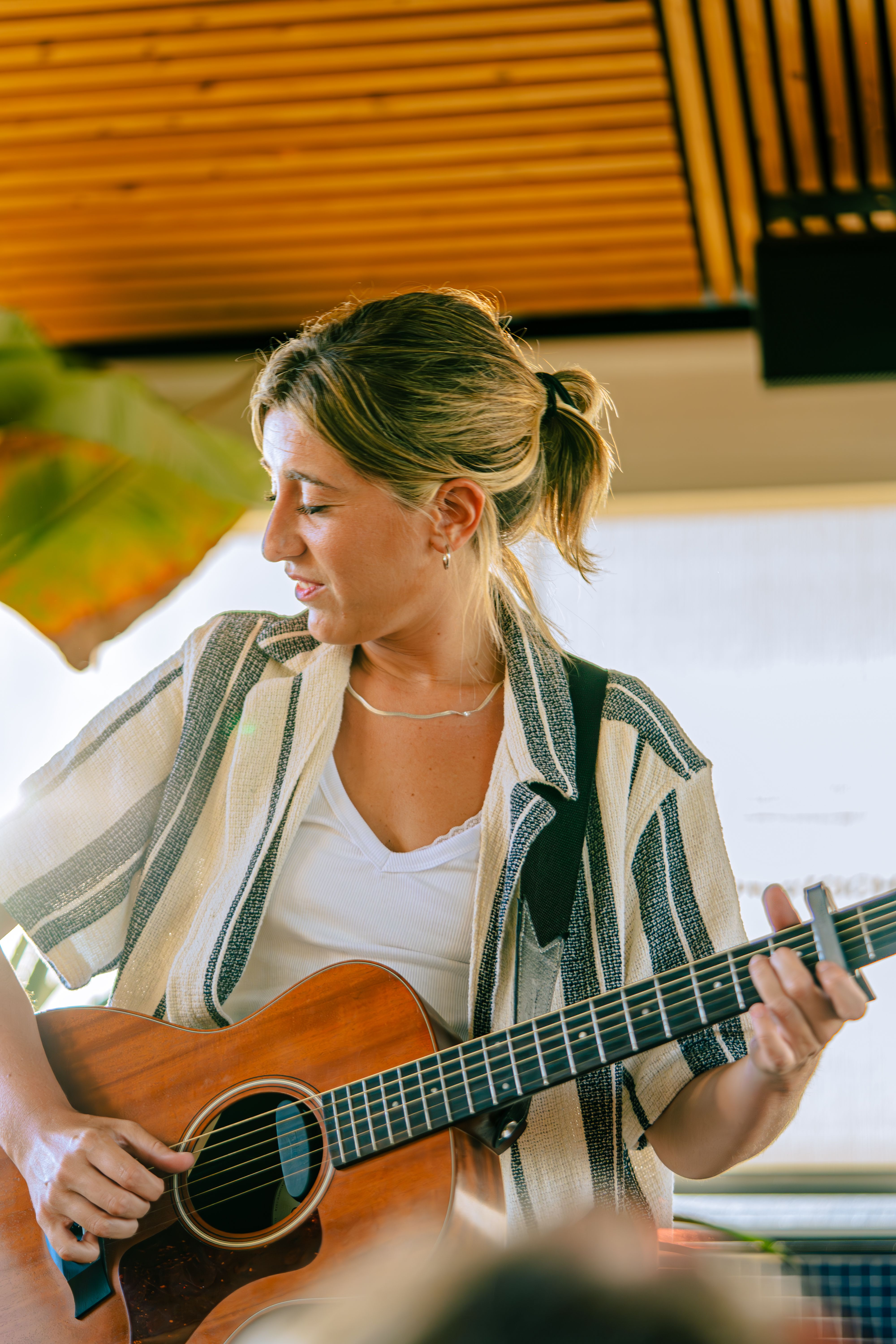 A smiling woman playing guitar indoors, capturing a lively and joyful moment.