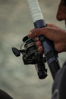 Detailed shot of a fisherman's hand holding a reel by the Atlantic Ocean in Tangier, Morocco.