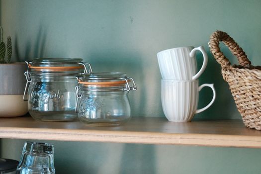 Modern kitchen shelf featuring glass jars and stacked white mugs, ideal for interior decor.