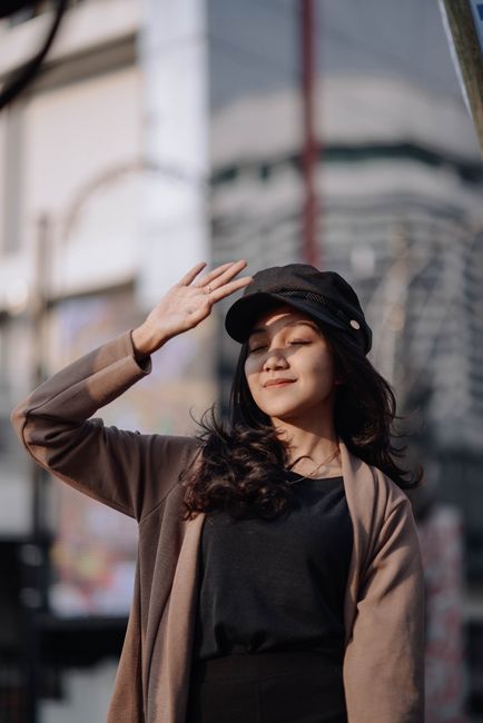 Asian woman in casual fashion posing outdoors in sunlight.