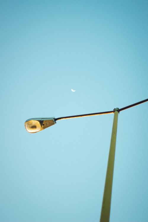 Free A streetlamp standing tall against a clear blue sky with a crescent moon in the background. Stock Photo
