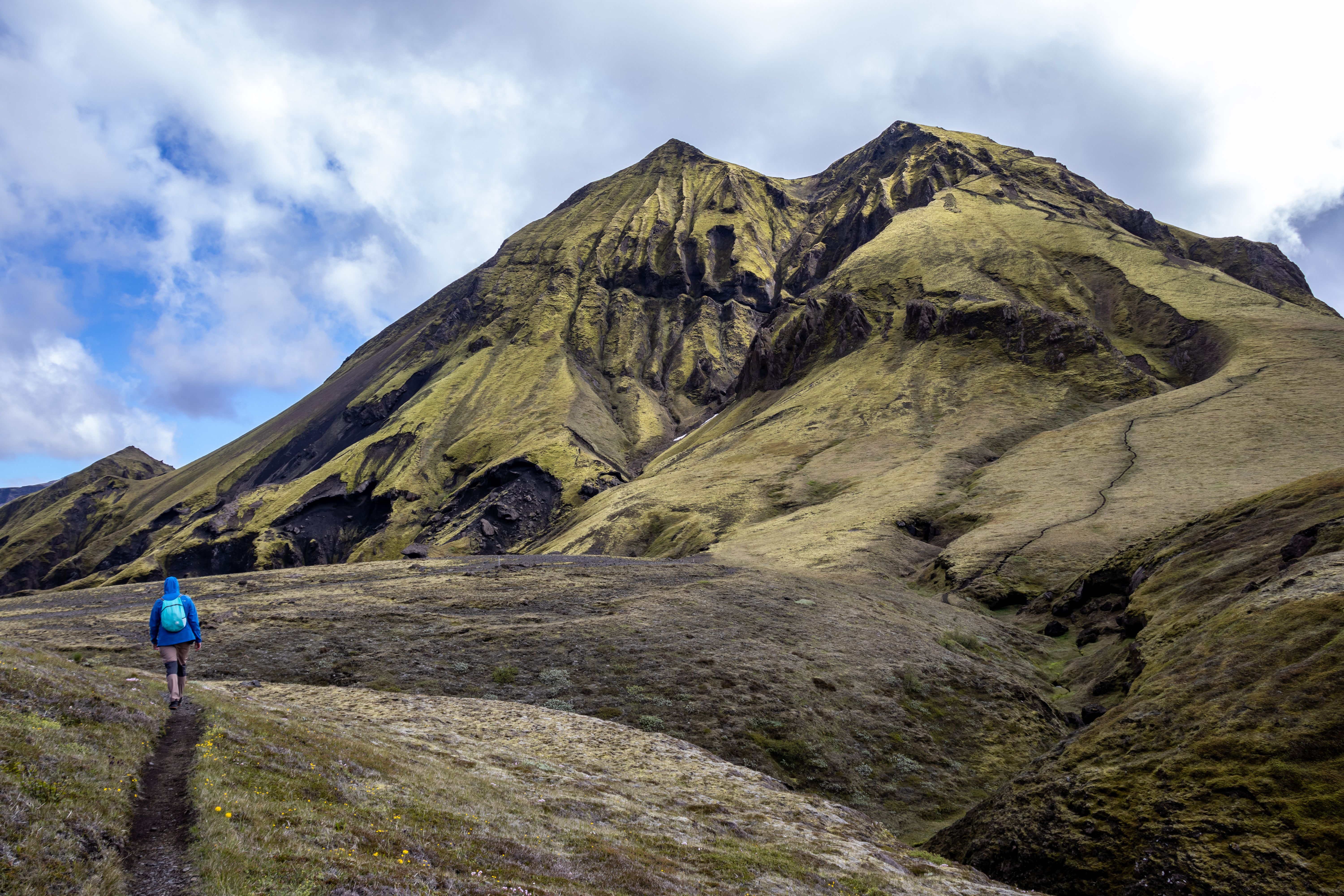 Hiker on a dramatic mountain trail with rugged terrain and scenic views.
