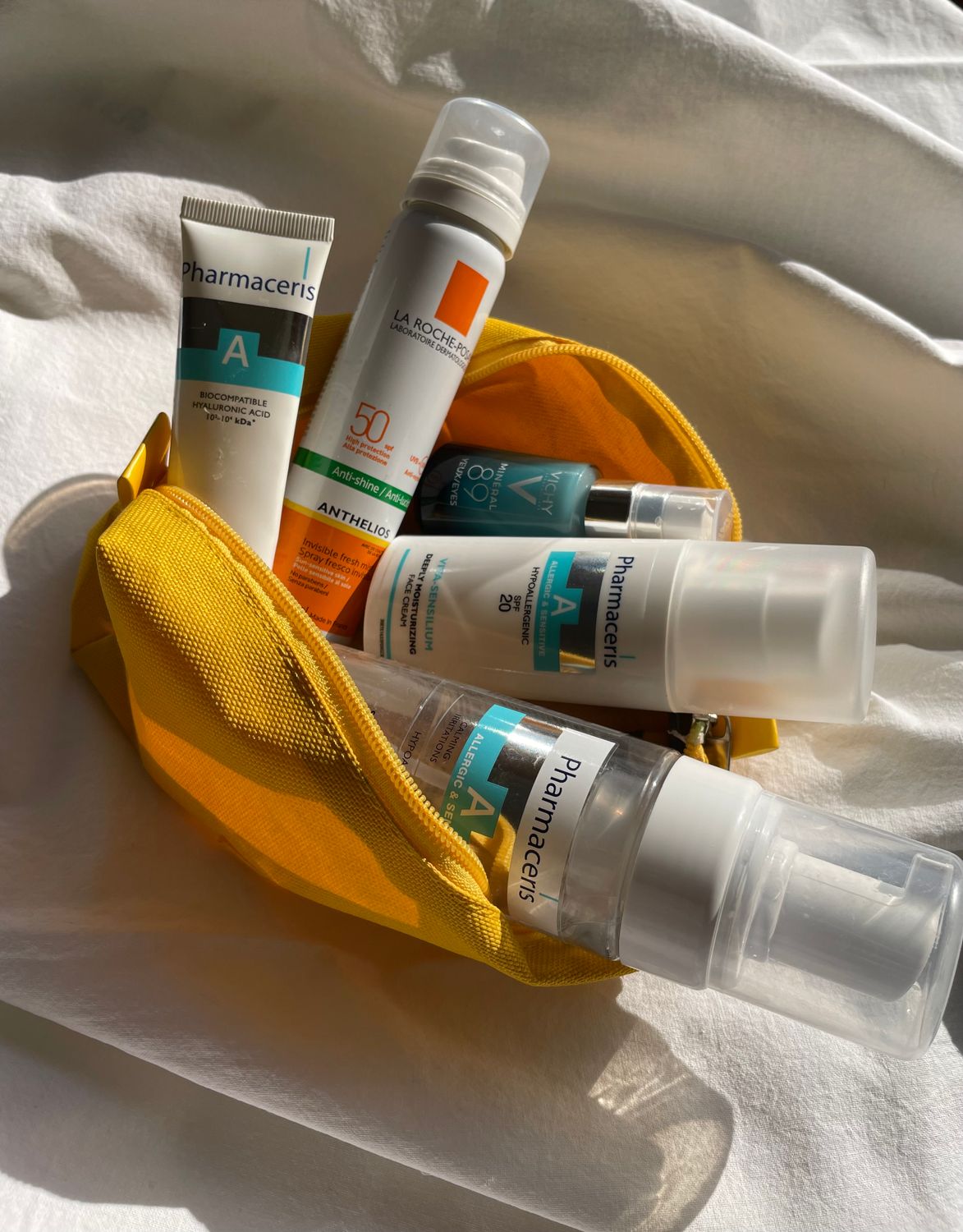 Assorted skincare products in a yellow travel pouch captured in natural lighting