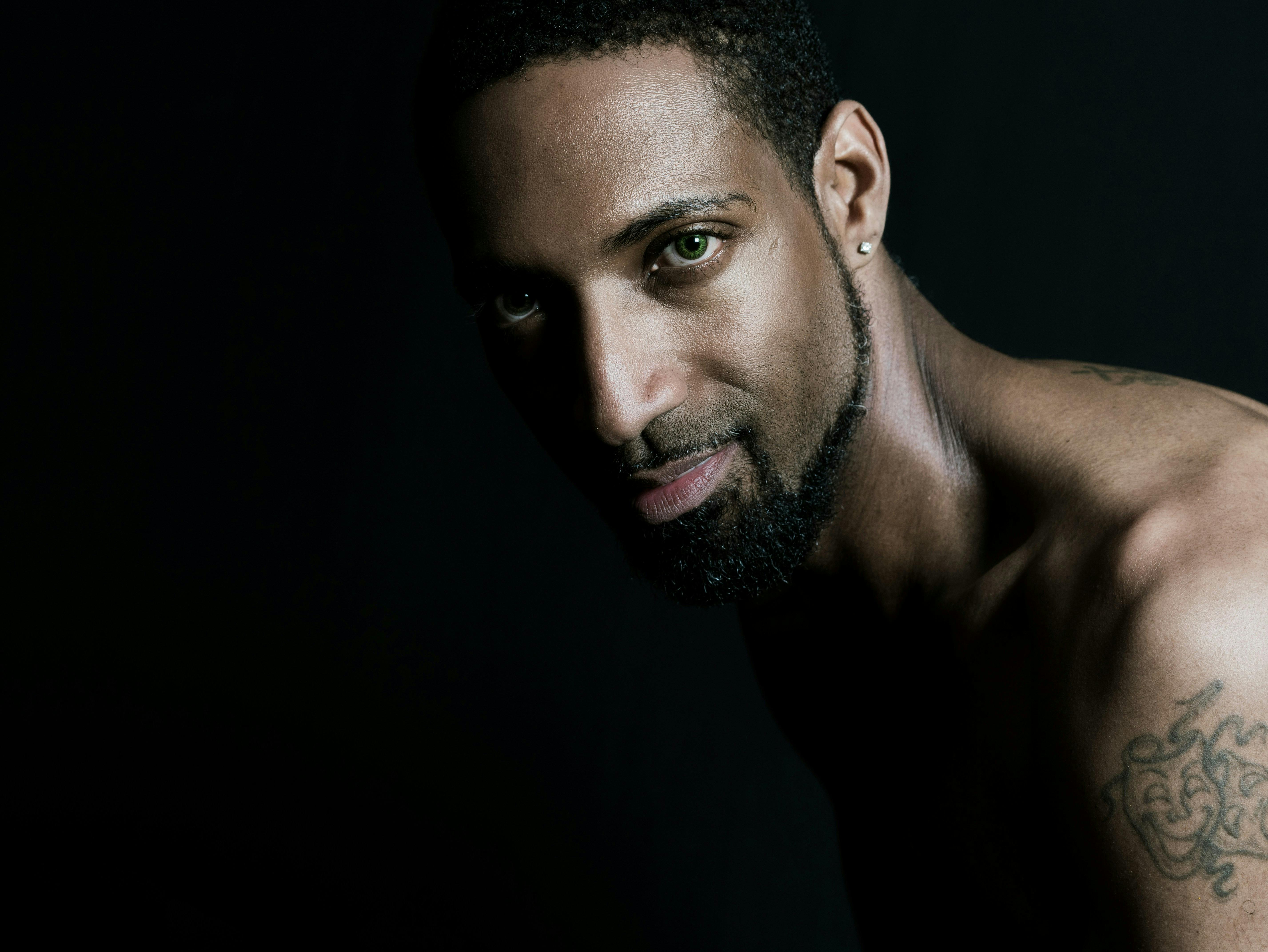 A confident man with a tattoo poses in a studio setting, exuding strength and style.
