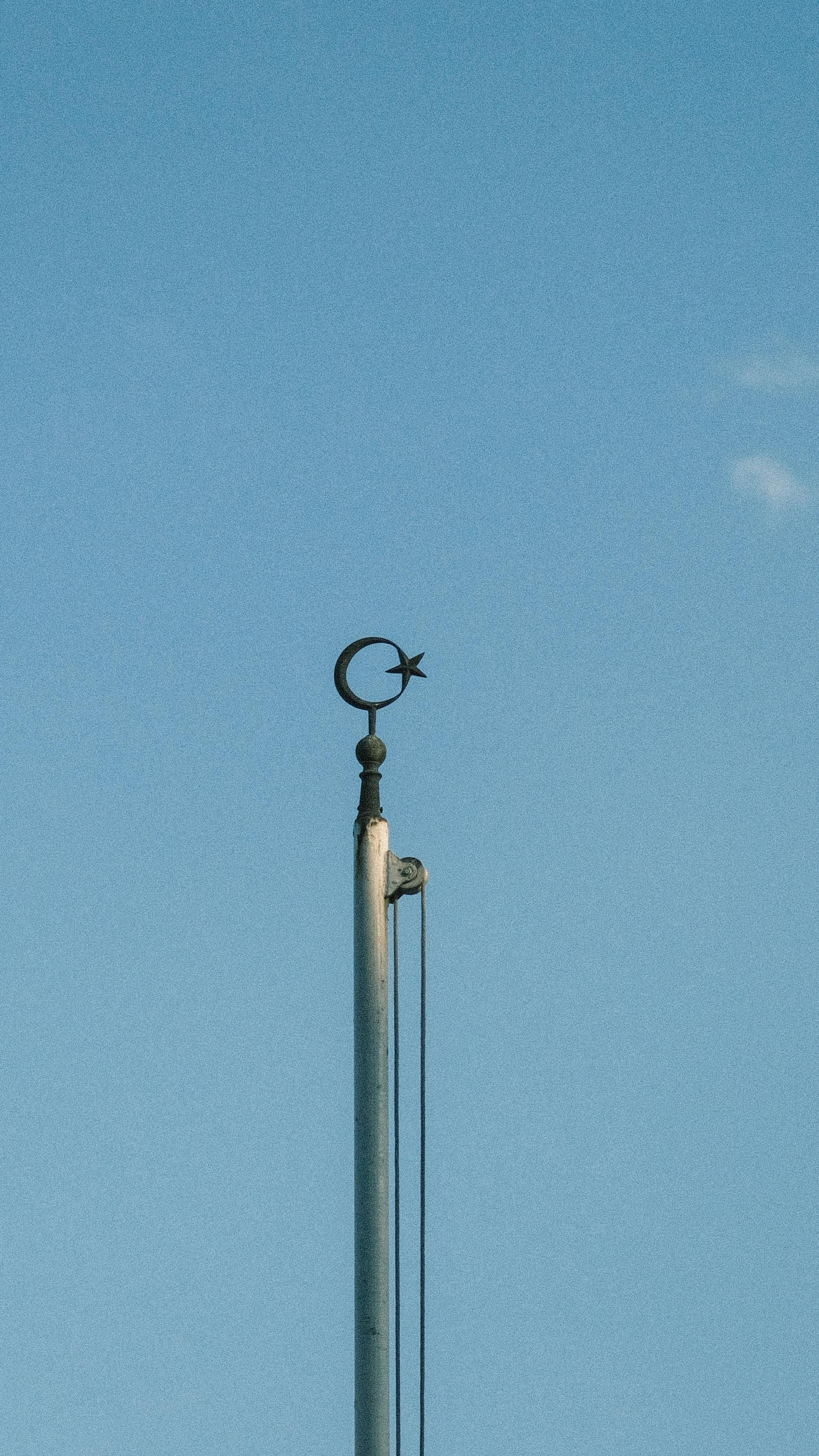 A crescent and star symbol atop a flagpole against a vibrant blue sky, symbolizing Islamic culture.