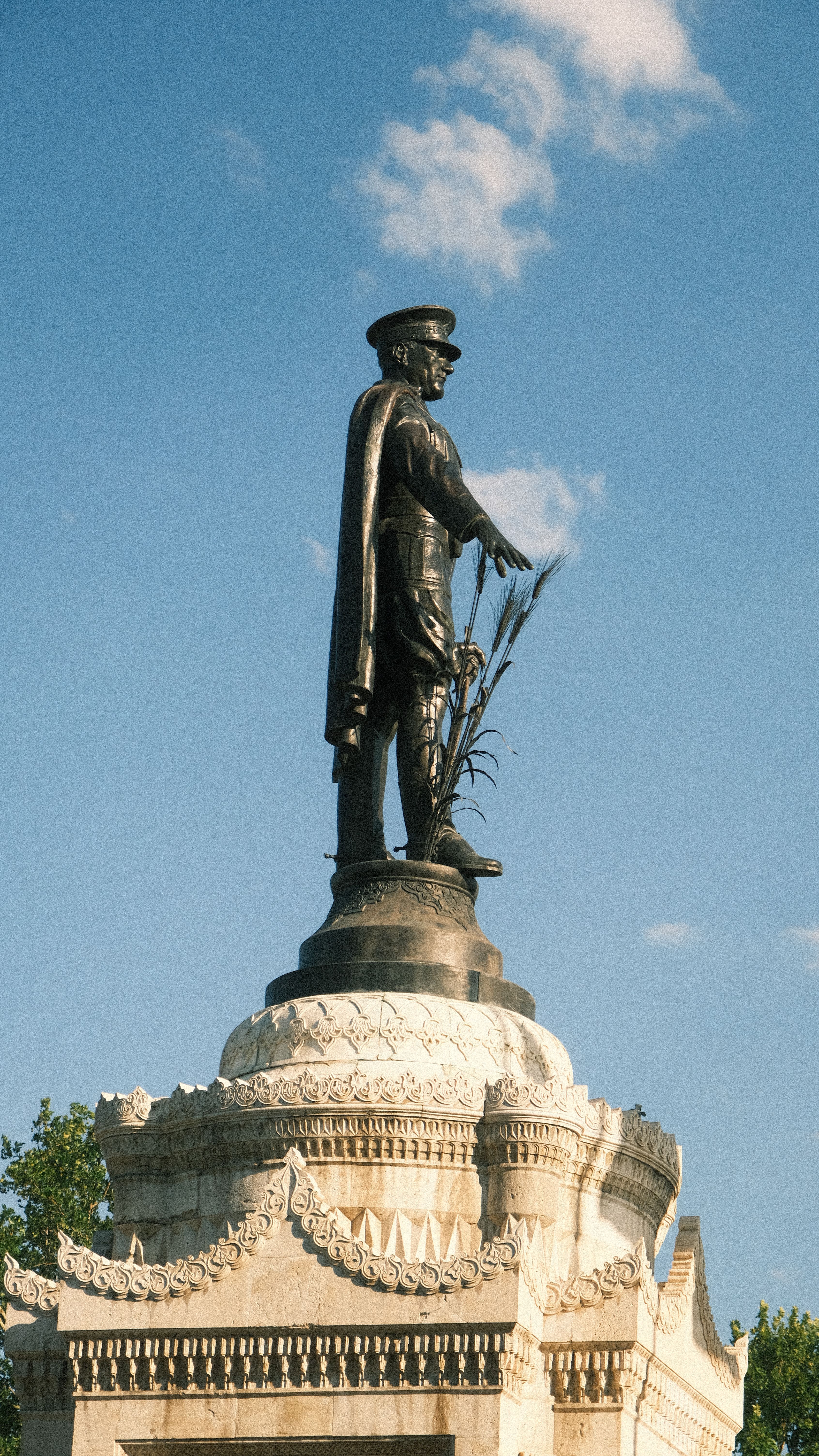 A majestic statue of a historic figure standing atop an ornate pedestal against a clear blue sky.