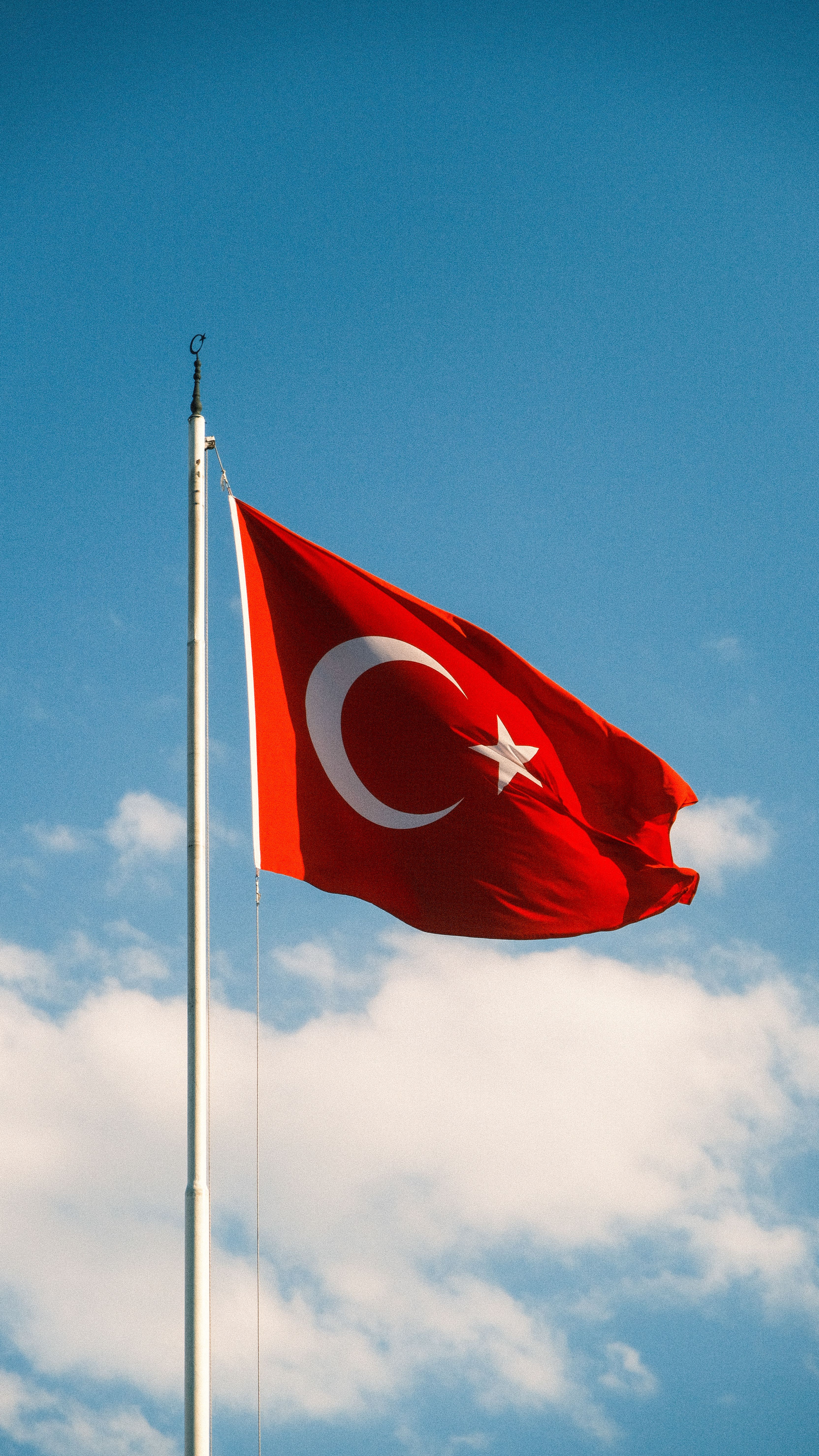 Turkish national flag on a flagpole against a clear blue sky symbolizing pride and identity.