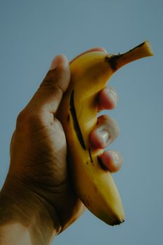 A hand firmly grasps a ripe banana against a vibrant blue sky, symbolizing health and tropical freshness.