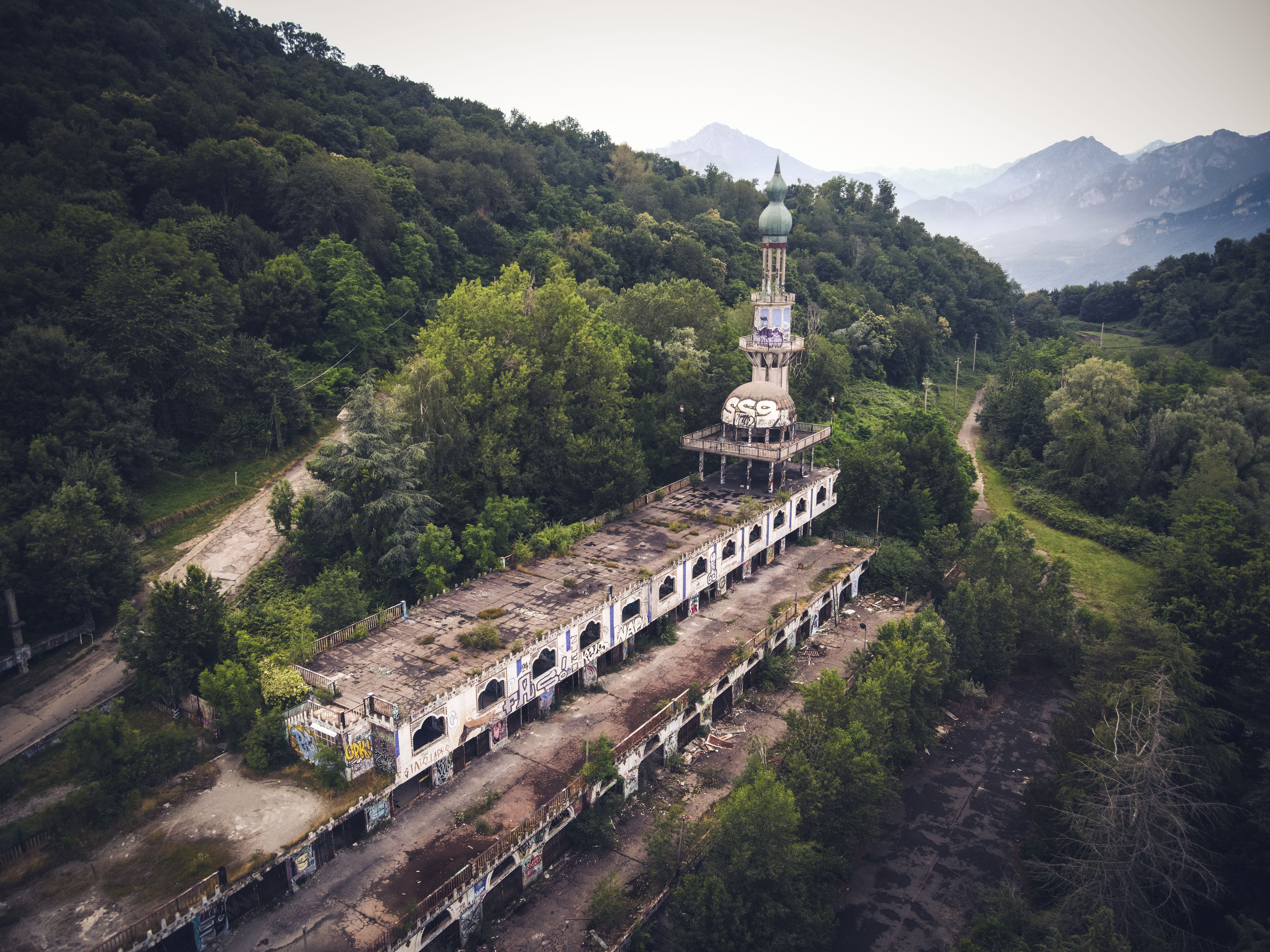 Drone shot of an abandoned monastery nestled in lush green hills with misty mountains in the background.